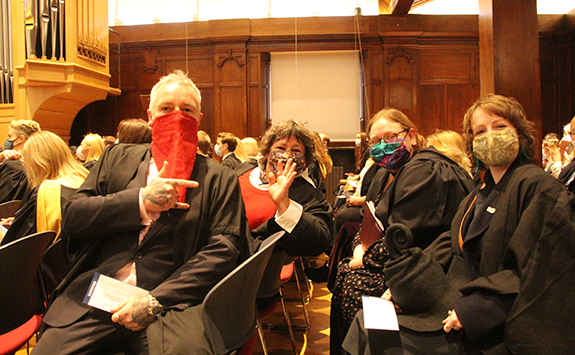Sue with friends in the graduation ceremony, all waving and wearing face masks